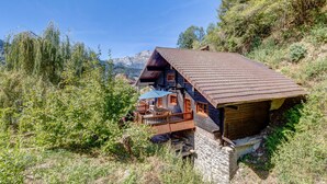 Una casa in legno rustica con tetto spiovente, fondamenta in pietra e un balcone che si affaccia su un paesaggio montuoso.