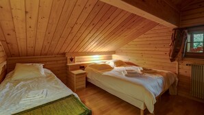 Camera da letto in una baita di legno con due letti, un comodino e una finestra con tende.