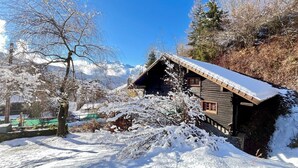 Una baita di legno con tetto spiovente, circondata da alberi coperti di neve e con montagne sullo sfondo.