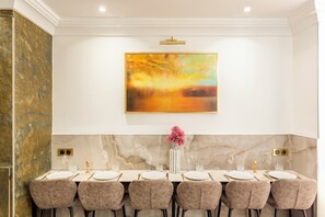 A dining area with a marble wall, a large abstract painting, and a vase with pink flowers. - Merveil - Luxury Suite - Louvre - Rousseau (Paris)