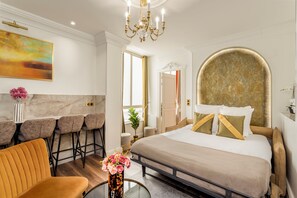 A modern hotel room with a large bed, a dining area with bar stools, and a chandelier. - Merveil - Luxury Suite - Louvre - Rousseau (Paris)