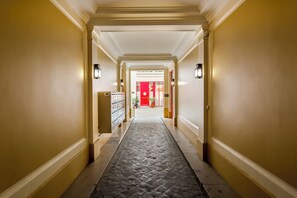 A hotel hallway with a tiled floor, yellow walls, and a red door at the end.