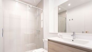 A modern bathroom with a glass-enclosed shower, a white toilet, and a wooden vanity with a sink and mirror. - Genteel Home Constitución IV (Seville)