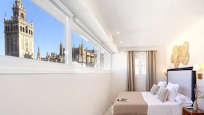 A hotel room with a large bed, a nightstand, a window with a view of a historic building, and a decorative wall piece. - Genteel Home Constitución IV (Seville)