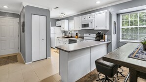 Een moderne keuken met witte kasten, een centraal eiland en een eethoek met een tafel en stoelen.