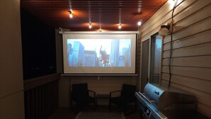 Een balkon met een plafondprojectiescherm waarop een stadsbeeld te zien is, een barbecue en twee stoelen.