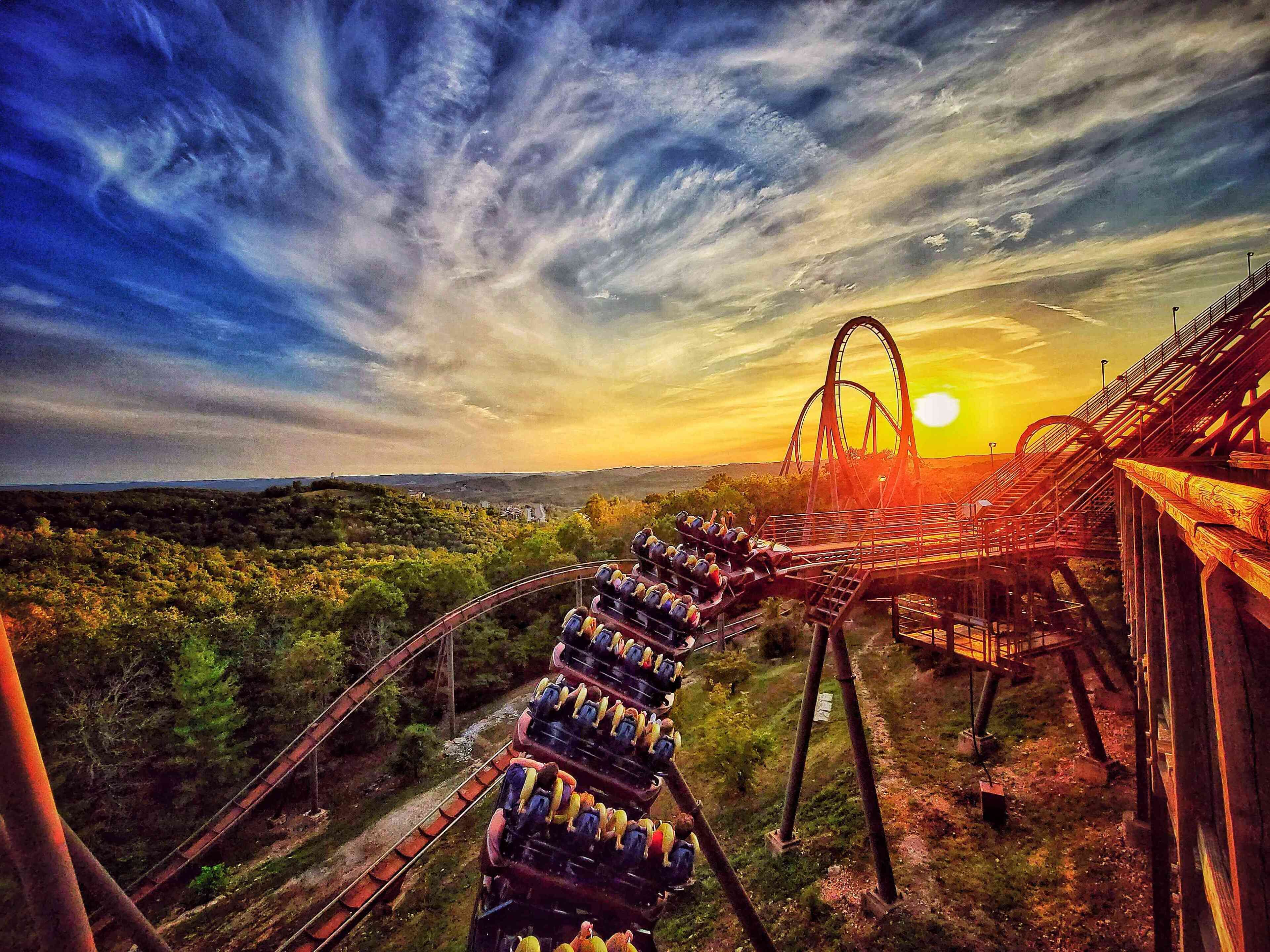 A roller coaster at sunset with tracks curving through a forested area.