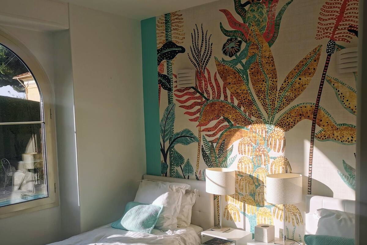 Ein Schlafzimmer mit Bett, Nachttischen, einer Lampe und einer Wandmalerei.