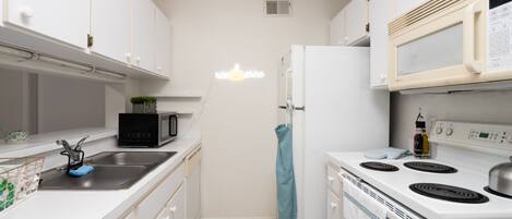 A compact kitchen with white cabinets, a black microwave, a white refrigerator, and a stove.