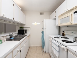Une cuisine de taille réduite avec des meubles blancs, un micro-ondes noir, un réfrigérateur blanc et une cuisinière.