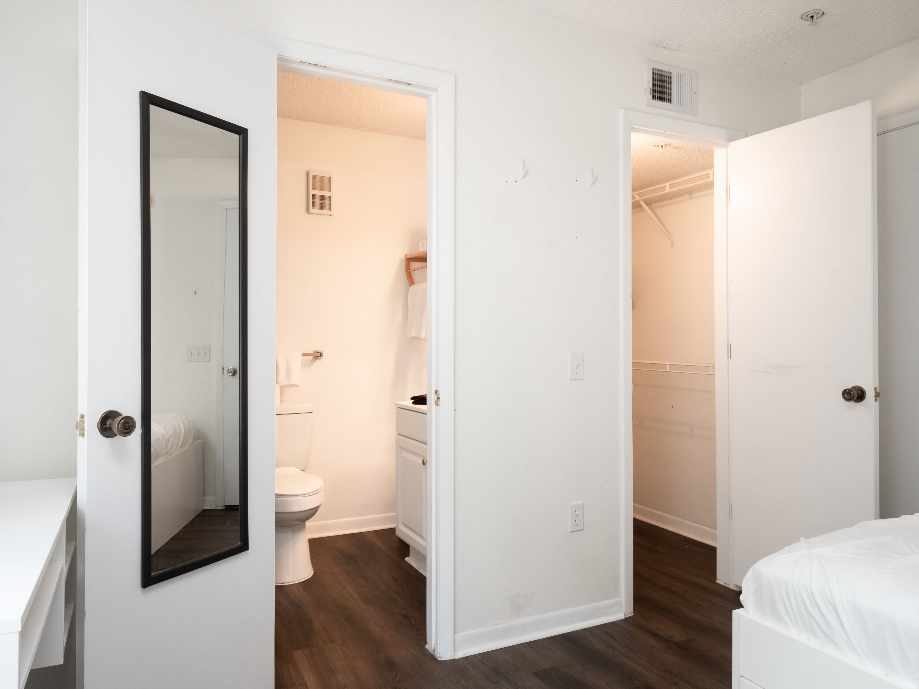Una habitación con una puerta, un inodoro, un lavabo y un espejo, todos de color blanco.
