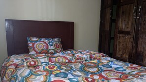 A bed with a colorful circular pattern bedspread and a matching pillow, a wooden headboard, and a wooden wardrobe. - Marthie Homeaway (Dodoma)