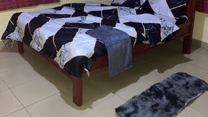 A bed with a patterned bedspread, a wooden headboard, and a grey rug on a tiled floor. - Marthie Homeaway (Dodoma)