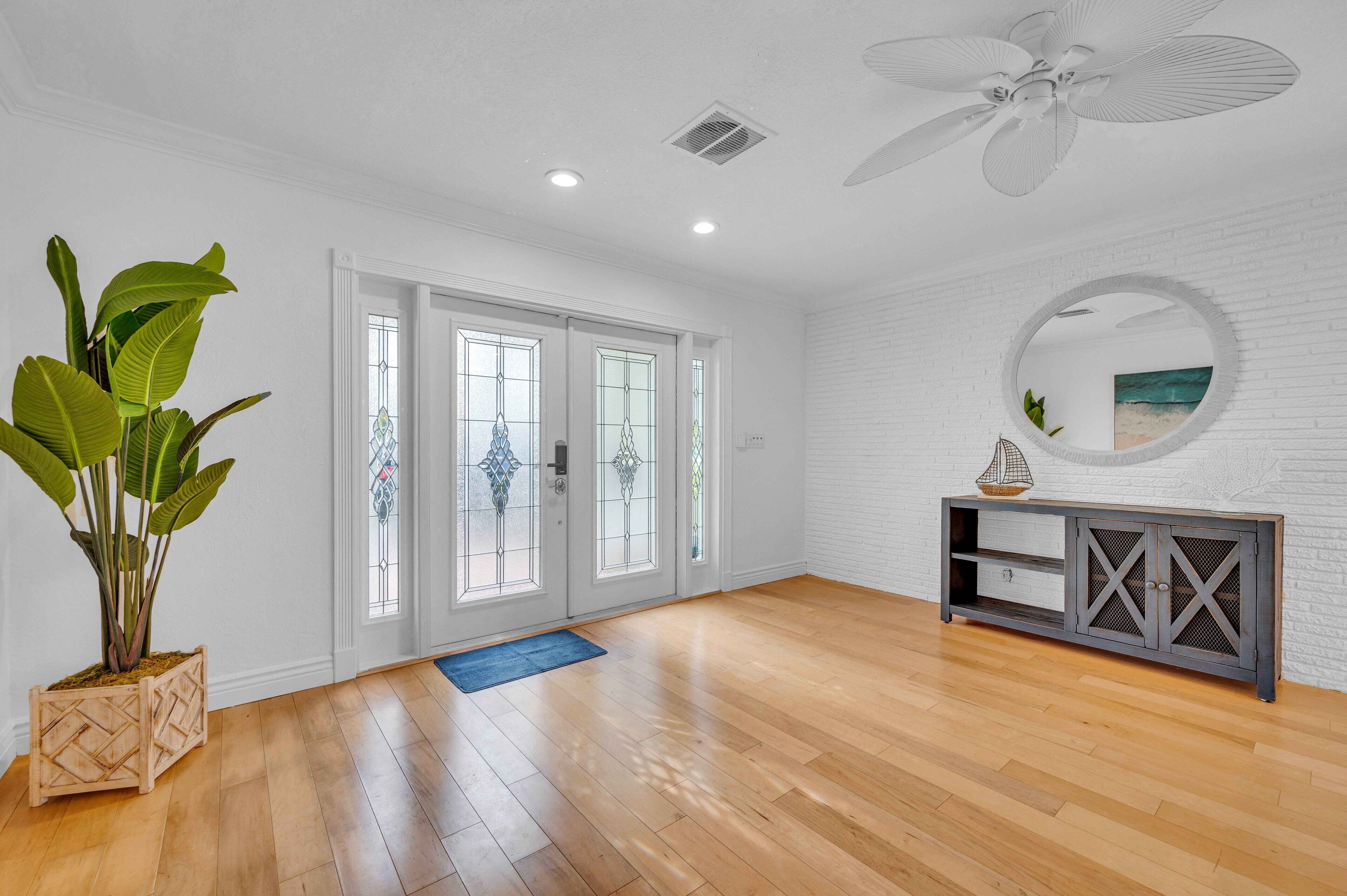 A spacious room with wooden flooring, a large potted plant, a round mirror, and a grey console table.