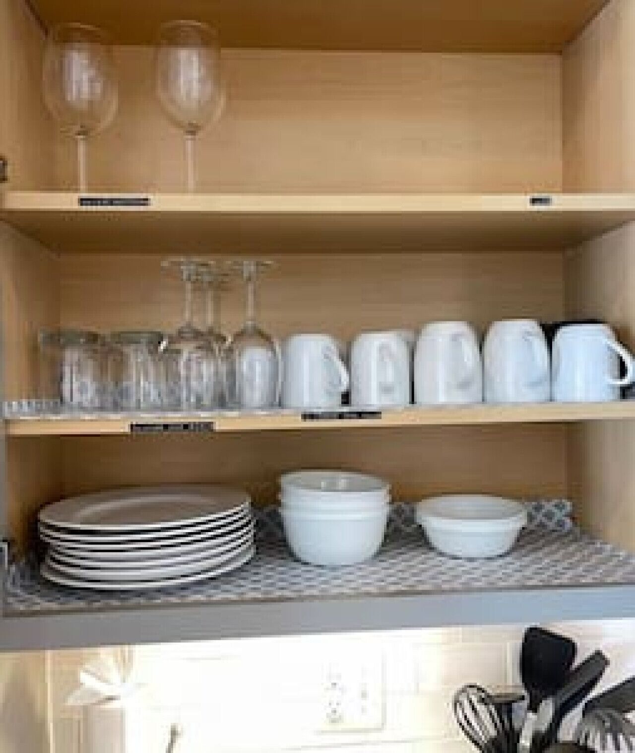 A kitchen with shelves holding wine glasses, cups, and plates.