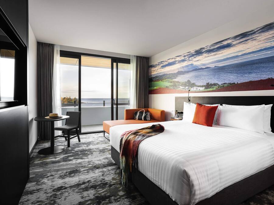 Une chambre d’hôtel avec un grand lit, un bureau, une chaise et une vue sur la mer par la fenêtre.