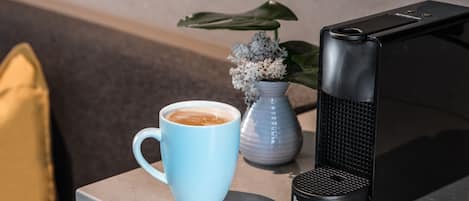 A coffee maker, a blue mug with coffee, a Breville coffee maker, and a small vase with flowers on a countertop.