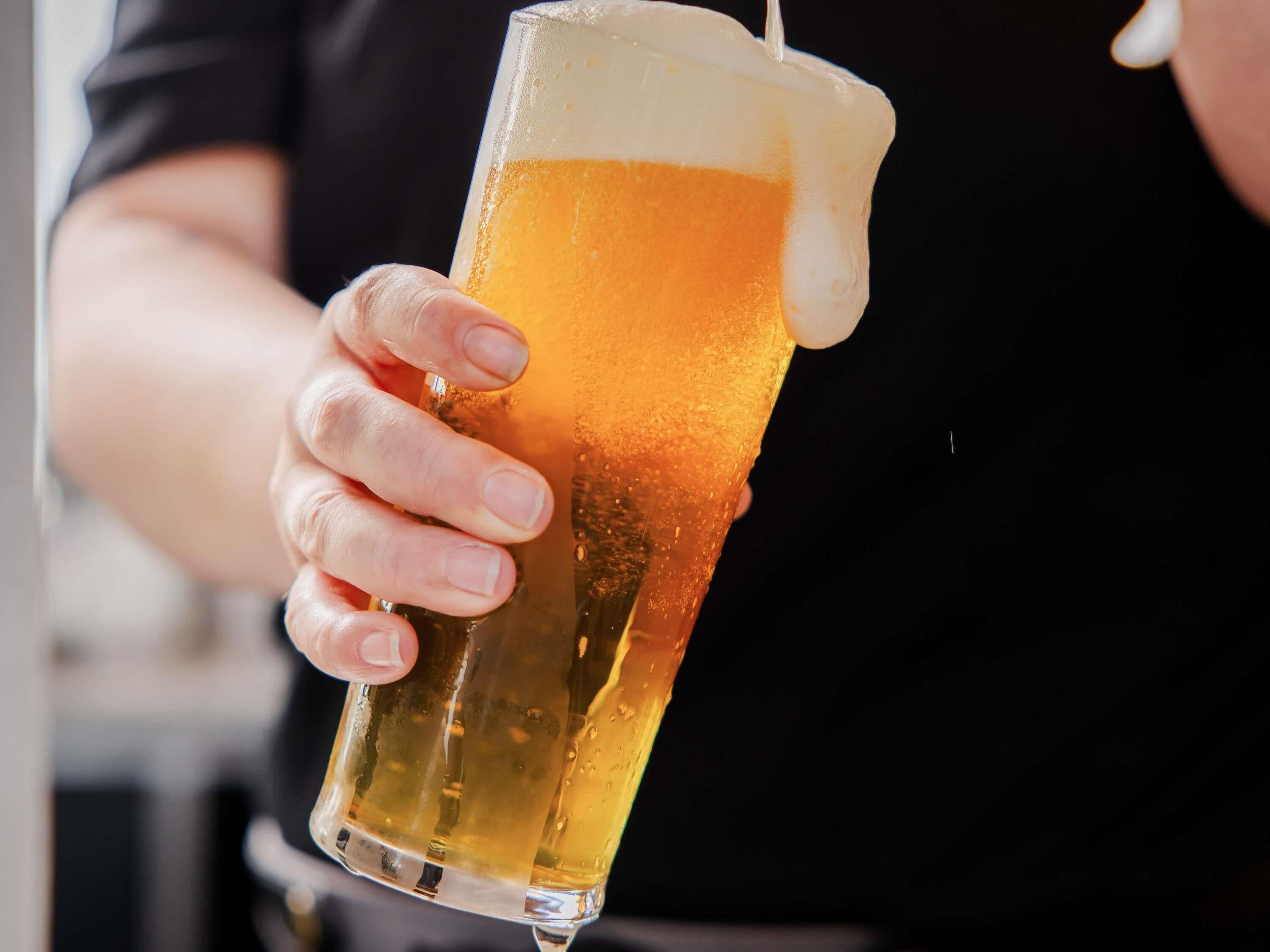 Eine Person hält ein hohes Glas Bier mit cremigem Schaum.