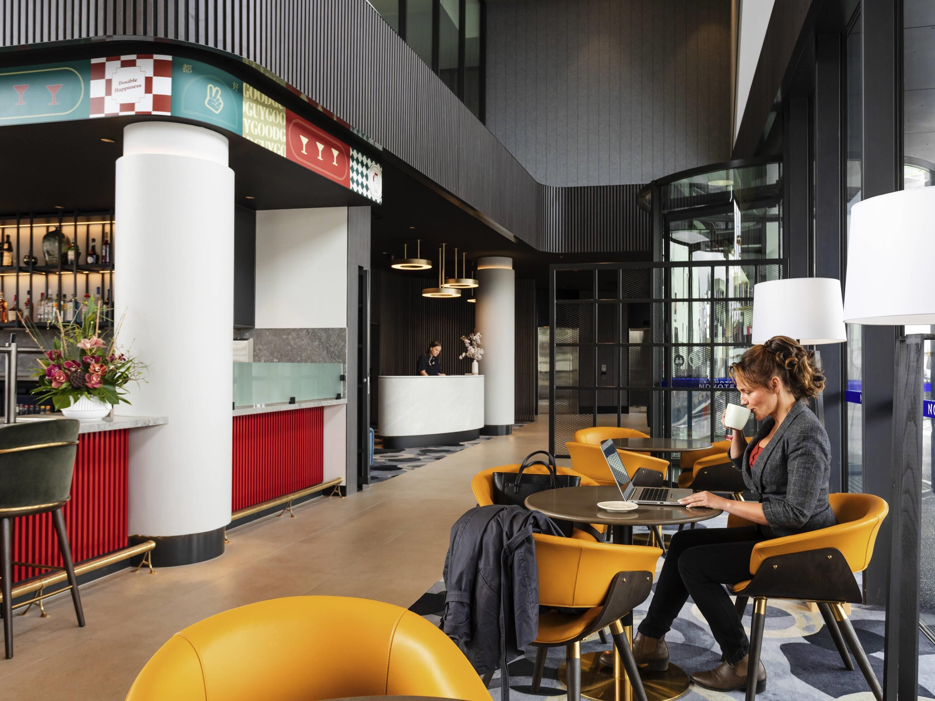 A modern hotel lobby with a reception desk, seating area, and a bar.