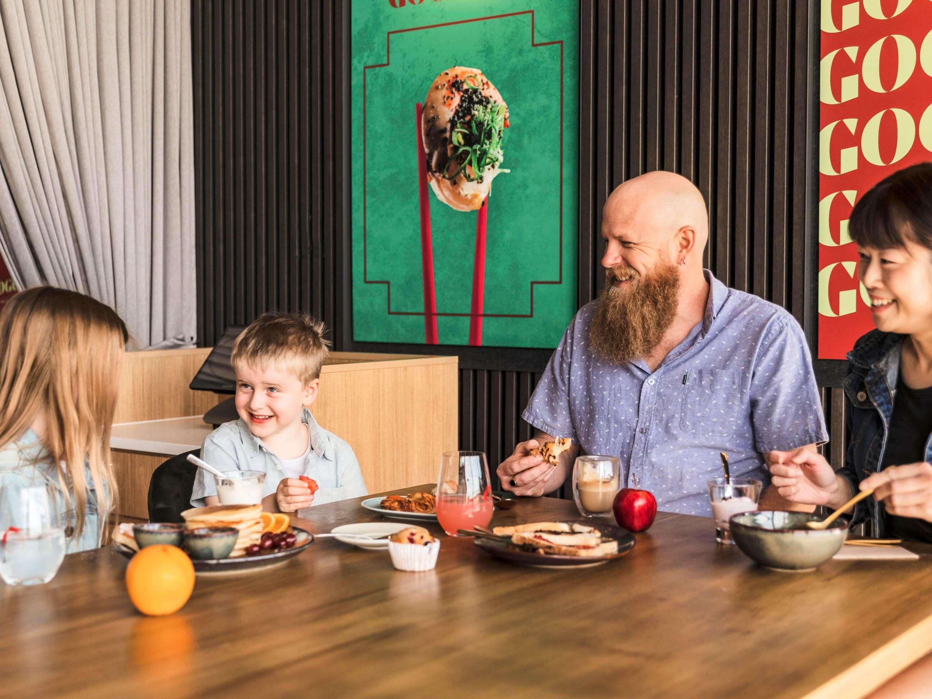 Una familia cenando en un restaurante con una decoración moderna, que incluye una mesa de madera y una pared verde con una línea roja.