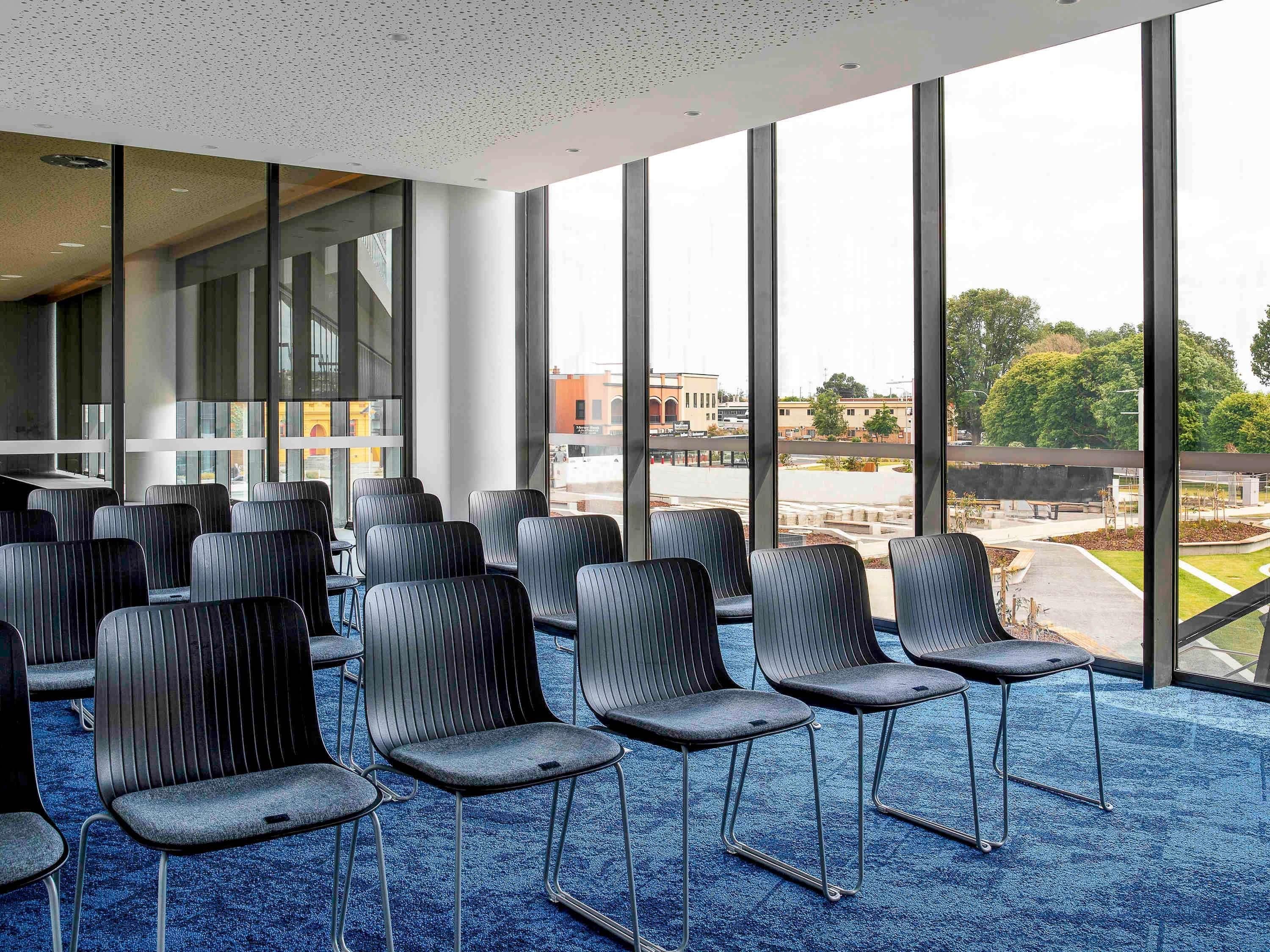 A conference room with rows of chairs, large windows, and a view of the cityscape.