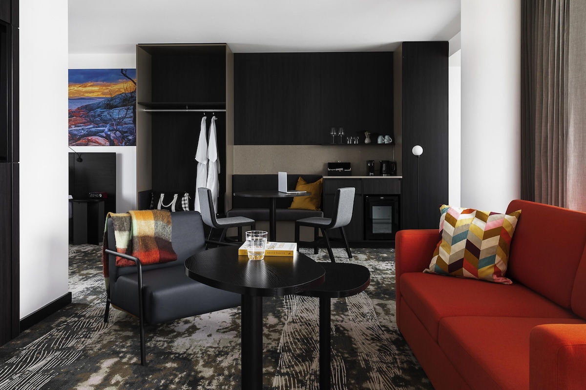 Una habitación de hotel moderna con sofá, sillón, mesa de comedor y kitchenette.