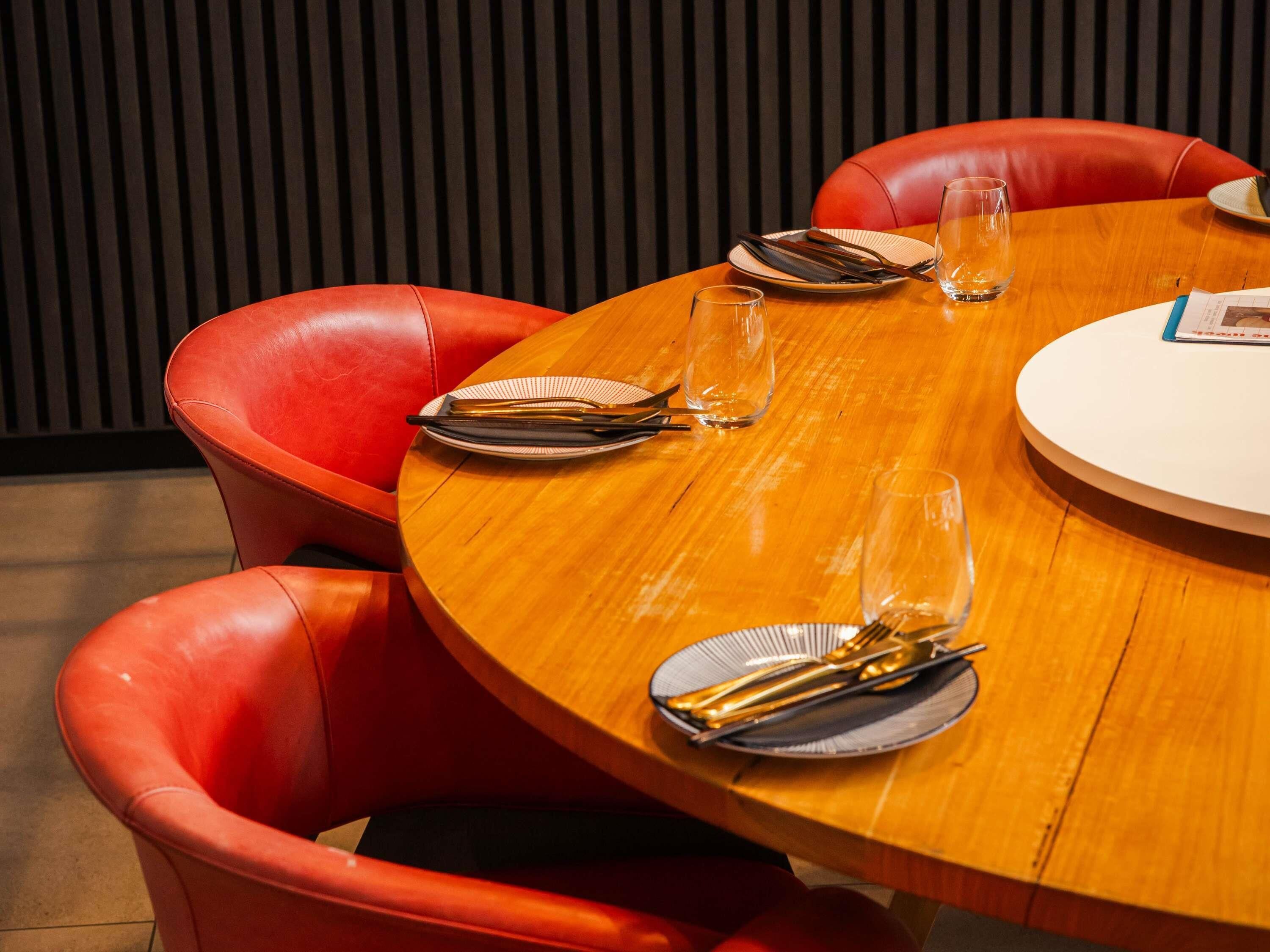 A round wooden table with a white placemat, surrounded by red leather chairs.