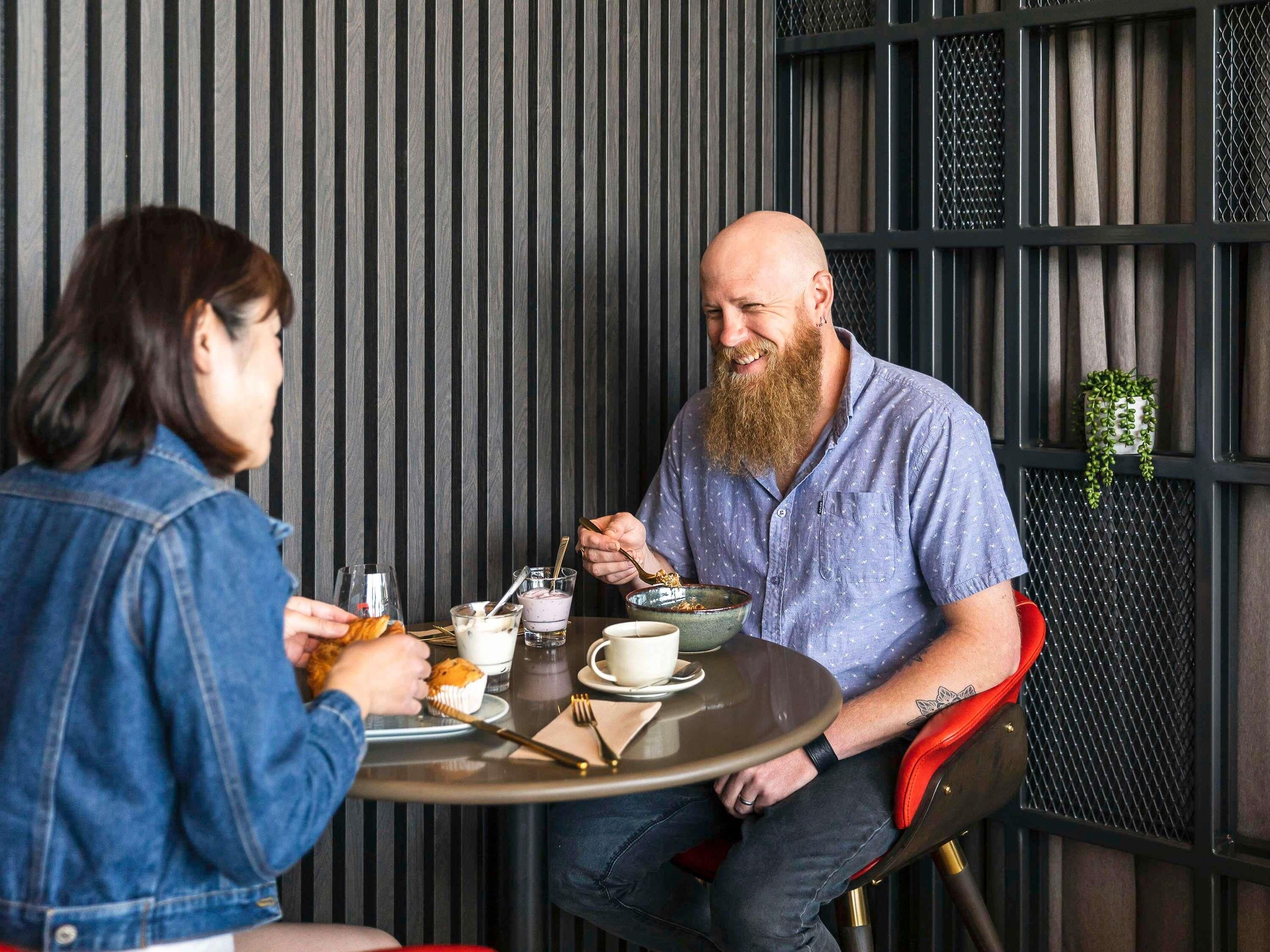 Two people dining at a table with a modern, industrial-style wall in the background.