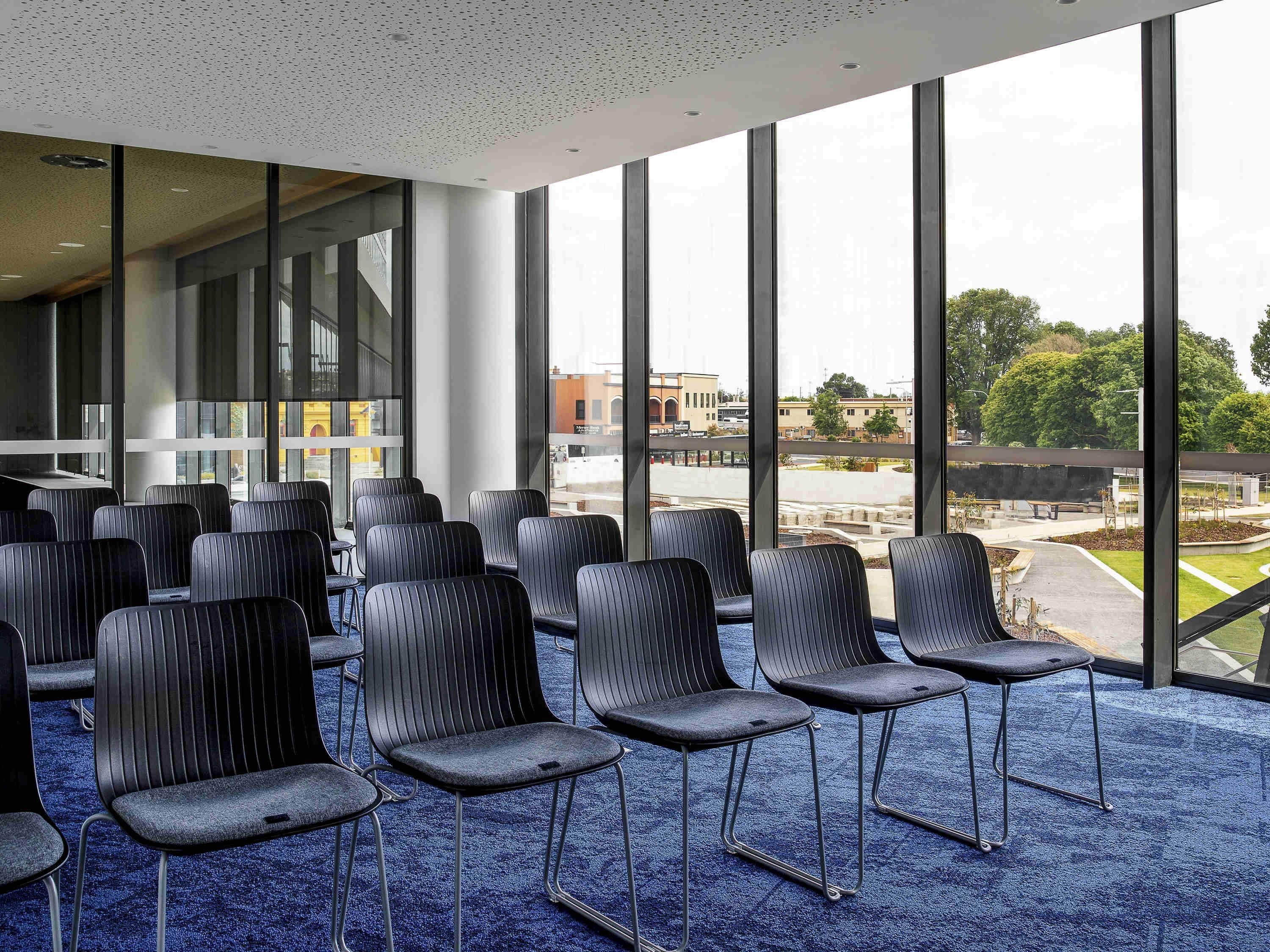 A conference room with rows of chairs, large windows, and a blue carpet.