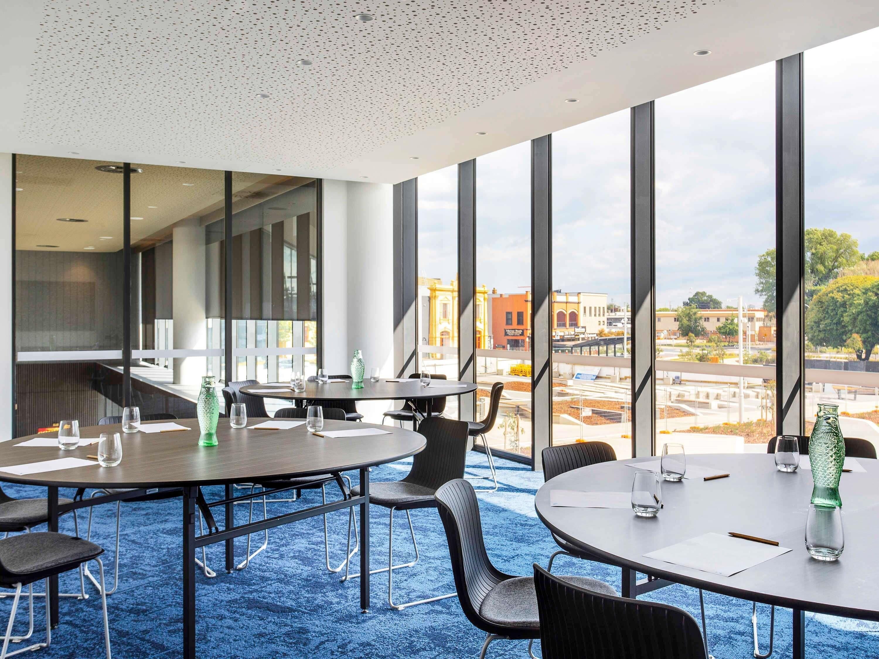 A conference room with large windows, a blue carpet, and a view of a cityscape.