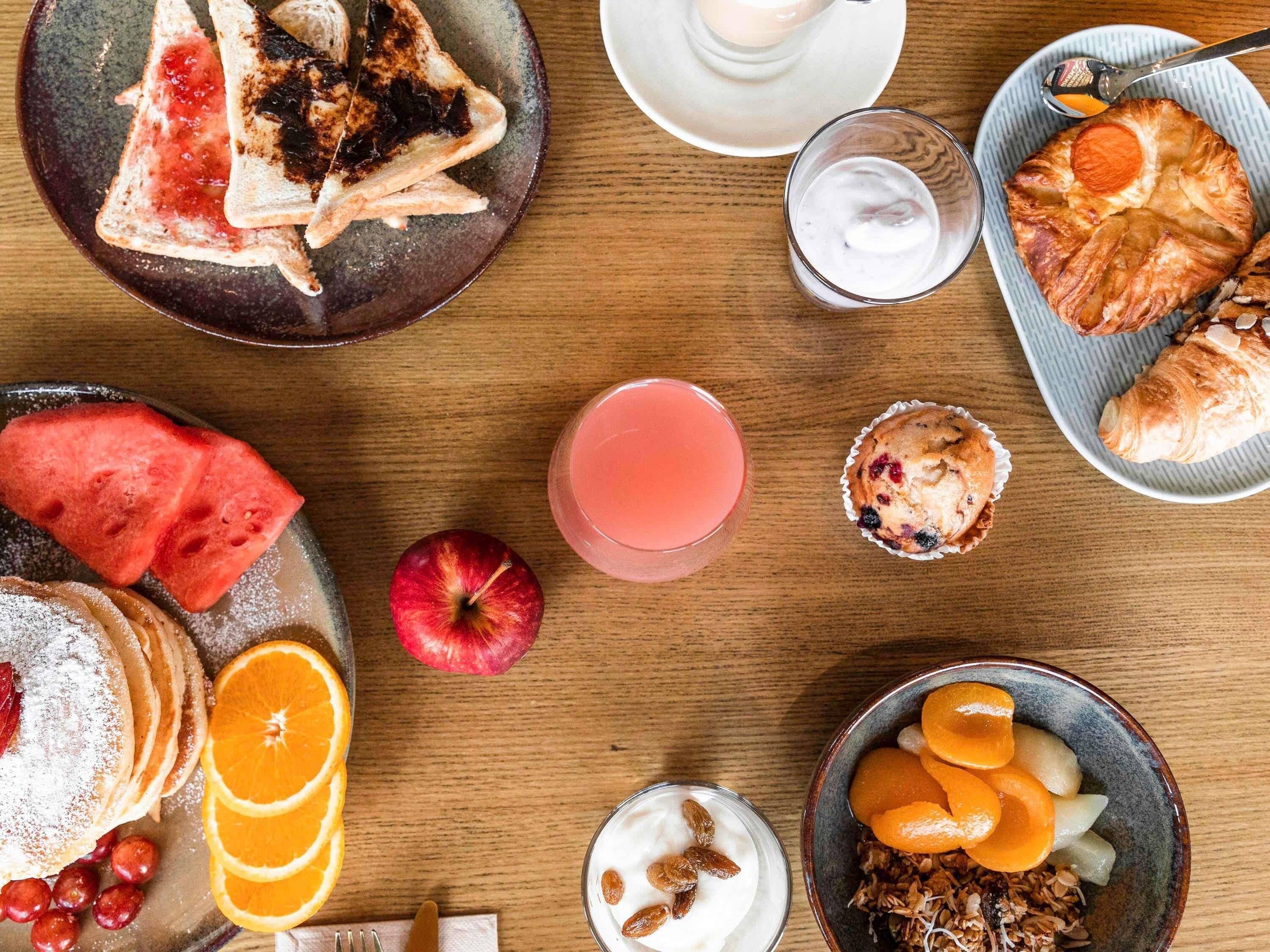Desayuno con tostadas, pasteles, fruta y un vaso de jugo.