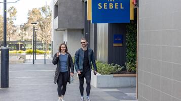 Dos personas caminando por una acera frente a un edificio con un letrero que dice "The Sebel".