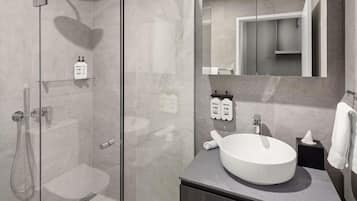 Un baño moderno con ducha envuelta en vidrio, lavamanos redondo y espejo sobre él.