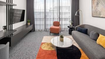 Uma sala de estar moderna com sofá, poltrona, mesa de centro e televisão na parede.