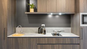 A modern kitchen with dark wood cabinets, a stainless steel sink, a coffee maker, and a plant on a shelf. - The Sebel Canberra Campbell (Campbell)