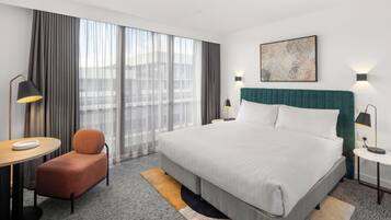 A hotel room with a large bed, a desk, a chair, and a window with curtains.