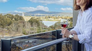 A person holding a wine glass, overlooking a scenic view with trees, a body of water, and distant hills. - The Sebel Canberra Campbell (Campbell)