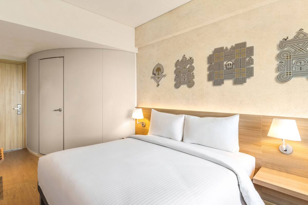 A hotel room with a large bed, a wardrobe, a TV, and decorative wall art.