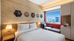 Habitación de hotel con una cama grande, mesitas de noche, un área de descanso y vistas a la ciudad.
