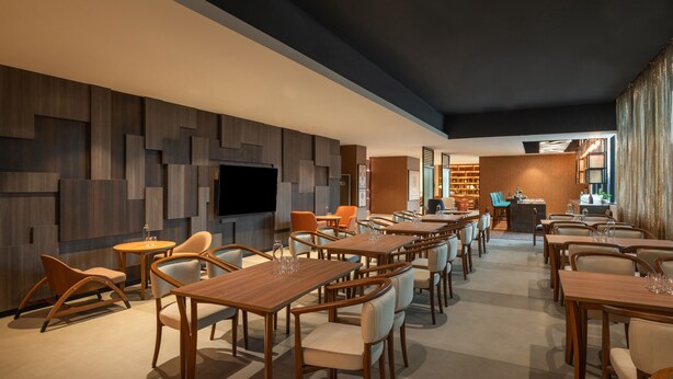Un restaurante moderno con mesas y sillas de madera, una zona de bar y un televisor en la pared.