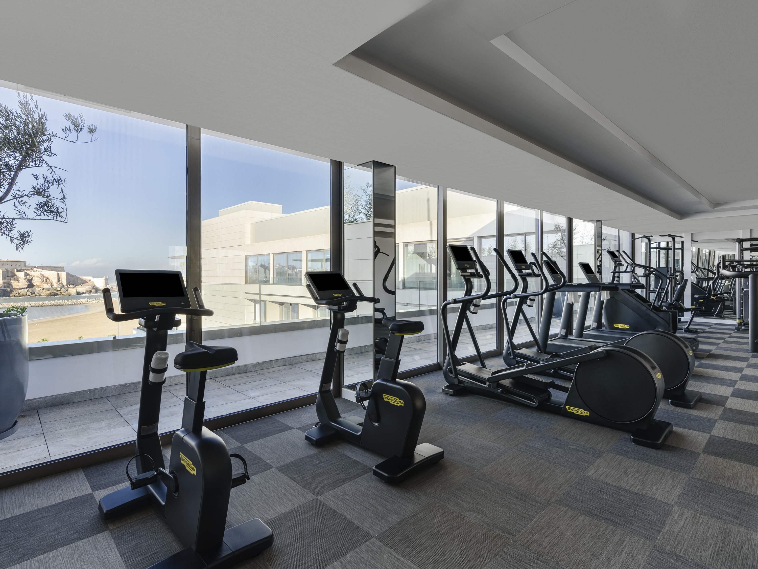 Ein modernes Fitnessstudio mit verschiedenen Cardiogeräten und großen Fenstern mit Blick auf die Stadtlandschaft.