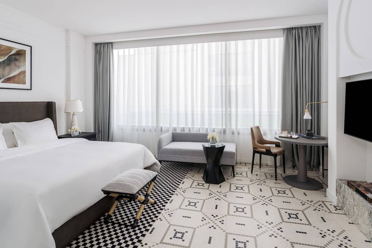 A hotel room with a large bed, a sofa, a small table with a lamp, and a TV mounted on the wall.