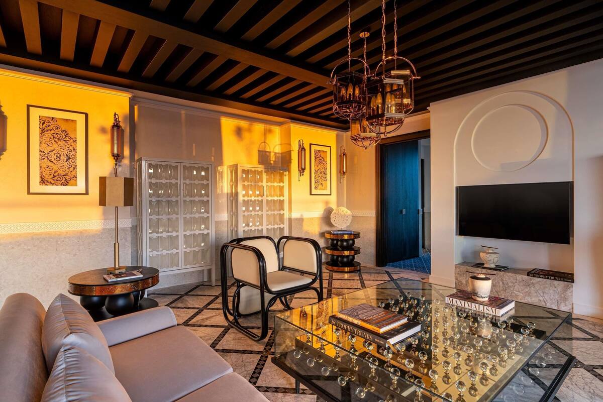 A modern living room with a sofa, chairs, a glass coffee table with trophies, a TV, and a bookshelf.
