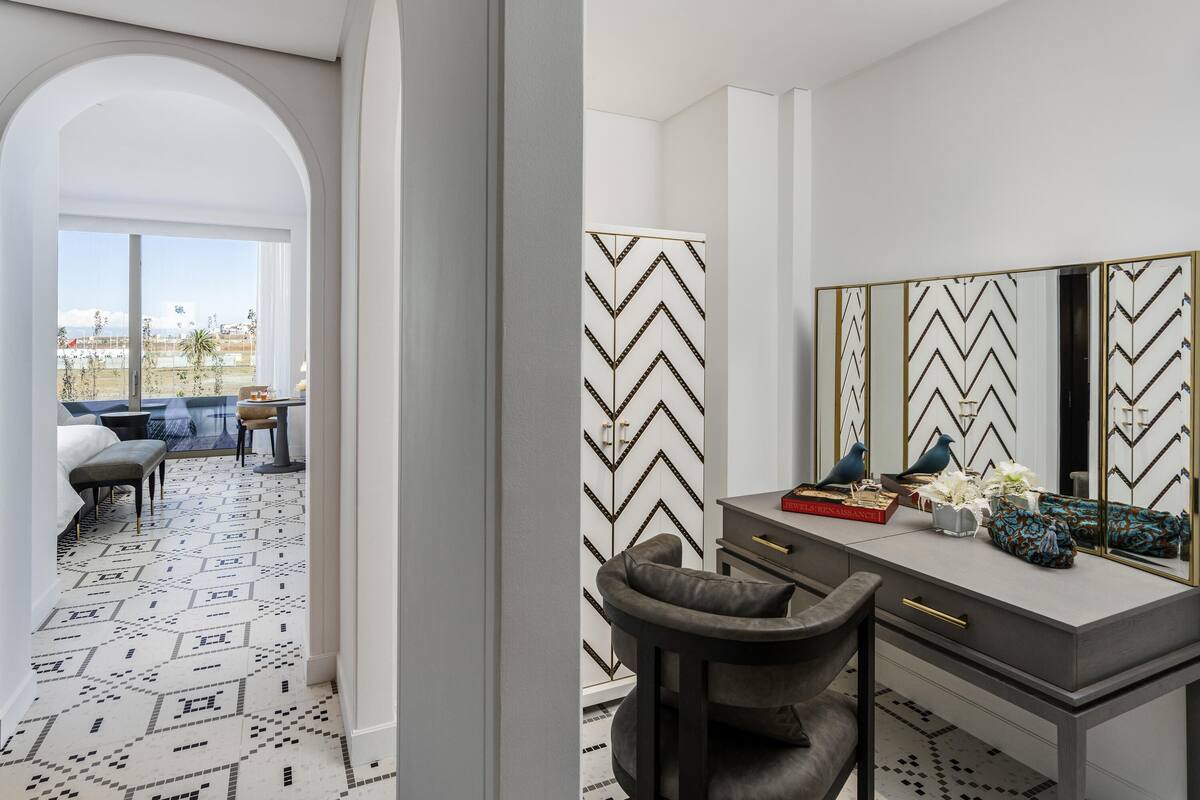 A modern bedroom with a large window, a vanity with a mirror, and a patterned floor.