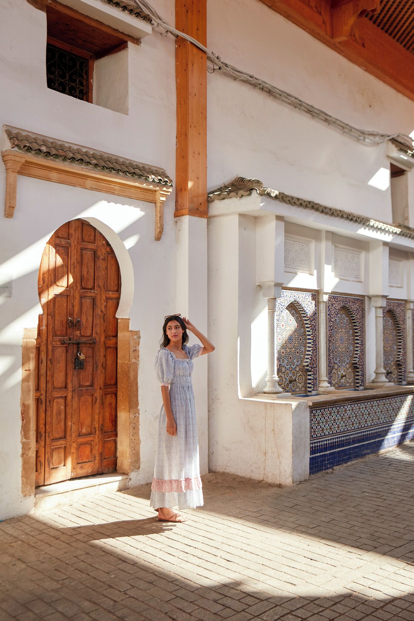 Uma mulher em frente a uma porta de madeira tradicional, com trabalhos detalhados em azulejos.