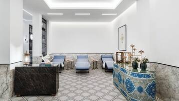 A modern spa area with a marble floor, a reception desk, and three lounge chairs.