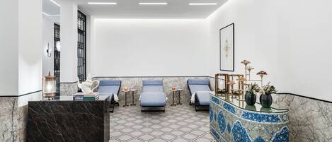 A modern spa area with a marble floor, a reception desk, and three lounge chairs.
