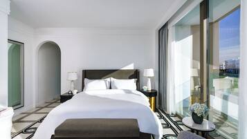 A hotel room with a large bed, a bedside table with a lamp, a small round table with a vase, and a view through a large window.