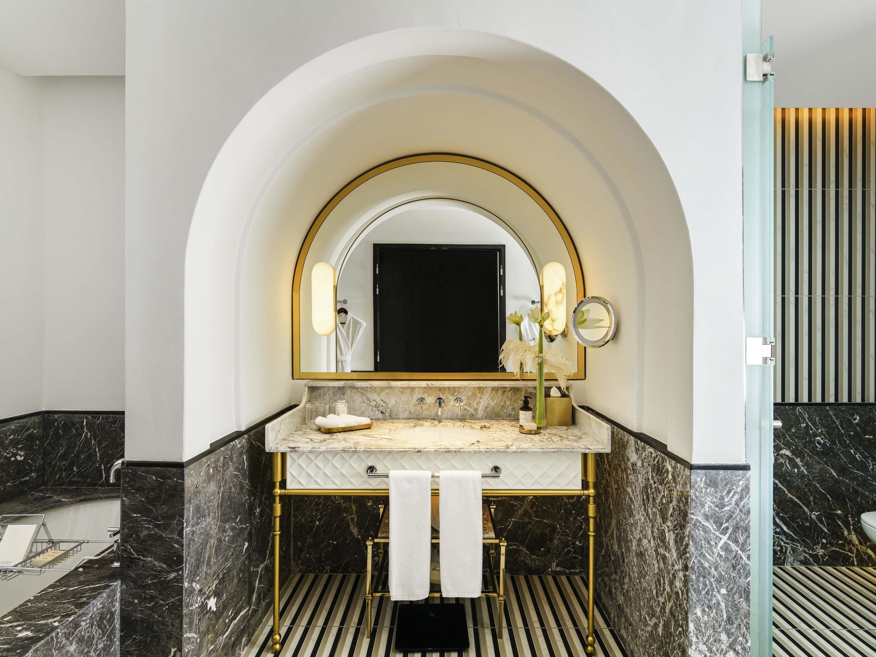 A modern bathroom with a marble vanity, gold fixtures, and a large mirror.
