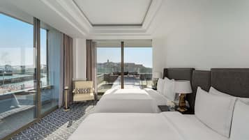 A hotel room with a large bed, a chair, a nightstand, and a view of a cityscape.